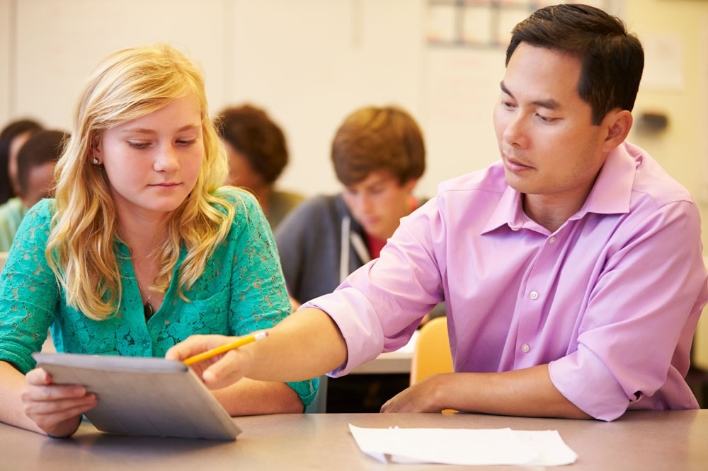 A male teacher helping a female high school student with an assignment